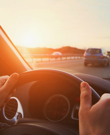 Conduite sur autoroute : voyage et coucher de soleil doré. Mains sur le volant d'une voiture, conduisant sur l'autoroute au coucher du soleil. Le soleil brille fortement à travers le pare-brise.