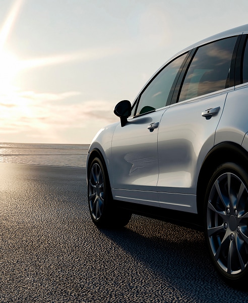 SUV de luxe blanc sur le sable au coucher du soleil SUV luxe blanc (type Cayenne) garé sur le sable mouillé face à l'océan. Coucher de soleil intense et reflets sur la carrosserie.
