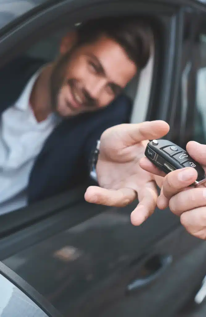 Remise de clés de voiture : La joie d'une transaction réussie. Remise des clés de voiture modernes. Un homme heureux en costume sort sa main du véhicule pour recevoir le boîtier.