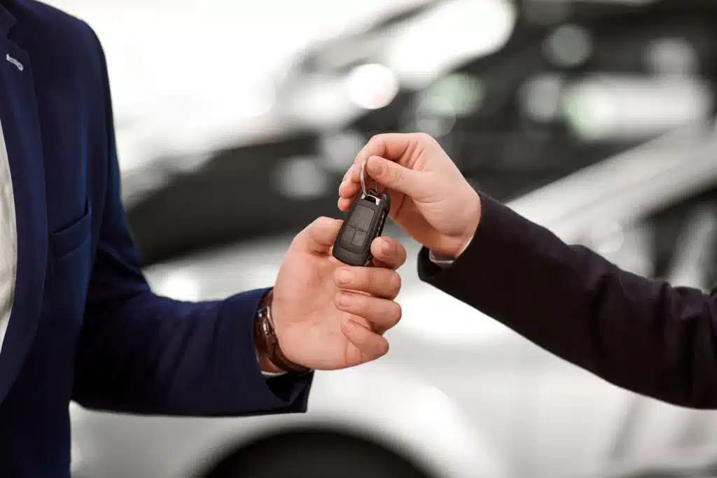 Clé de voiture : transaction et achat de votre nouveau véhicule. Remise d'une clé de voiture moderne entre deux professionnels en blazer. Transaction d'achat ou location de véhicule neuf dans un showroom.